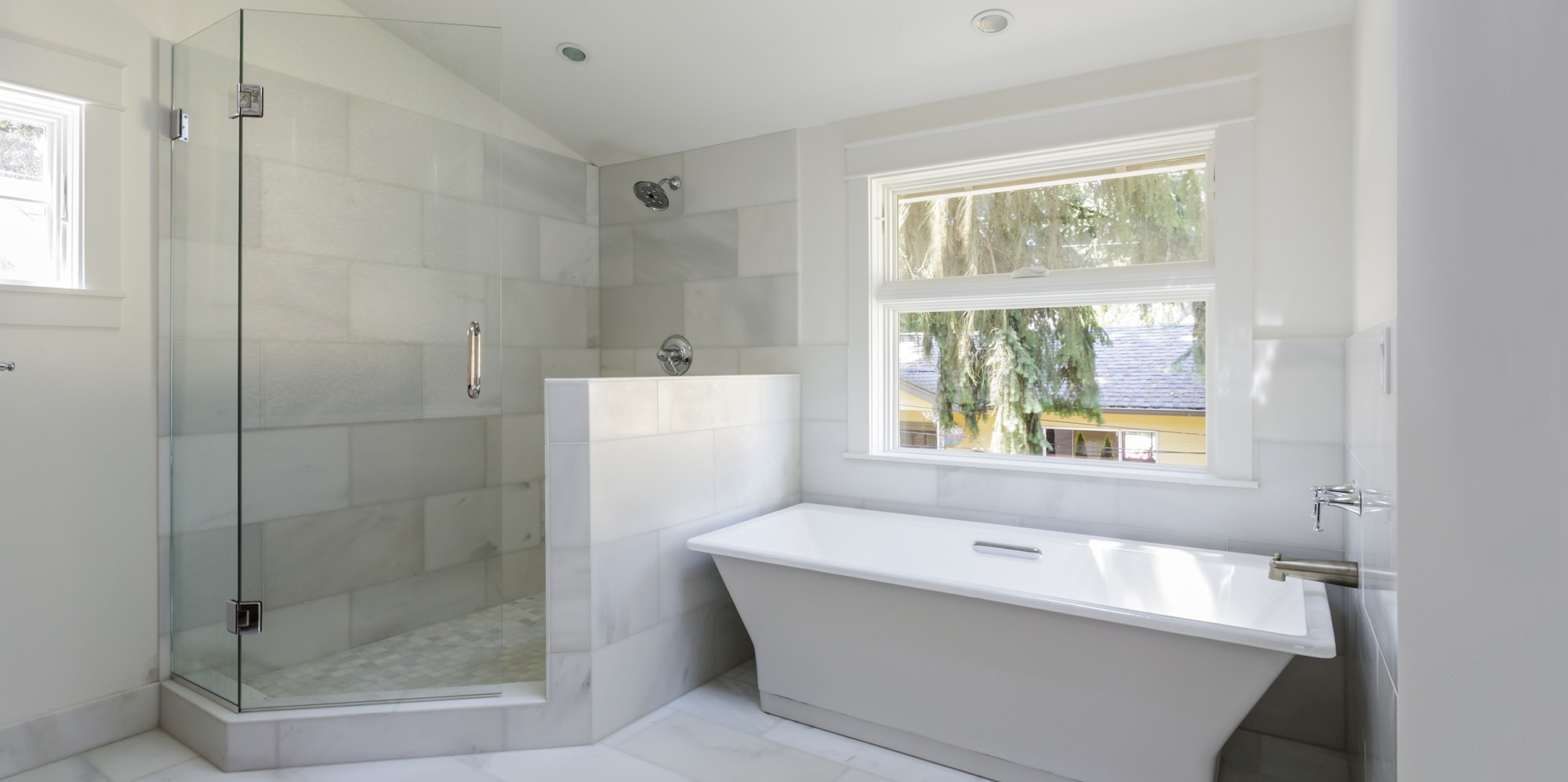 Modern bathroom featuring a walk-in glass shower and a freestanding white bathtub, with natural light from a window illuminating the space.