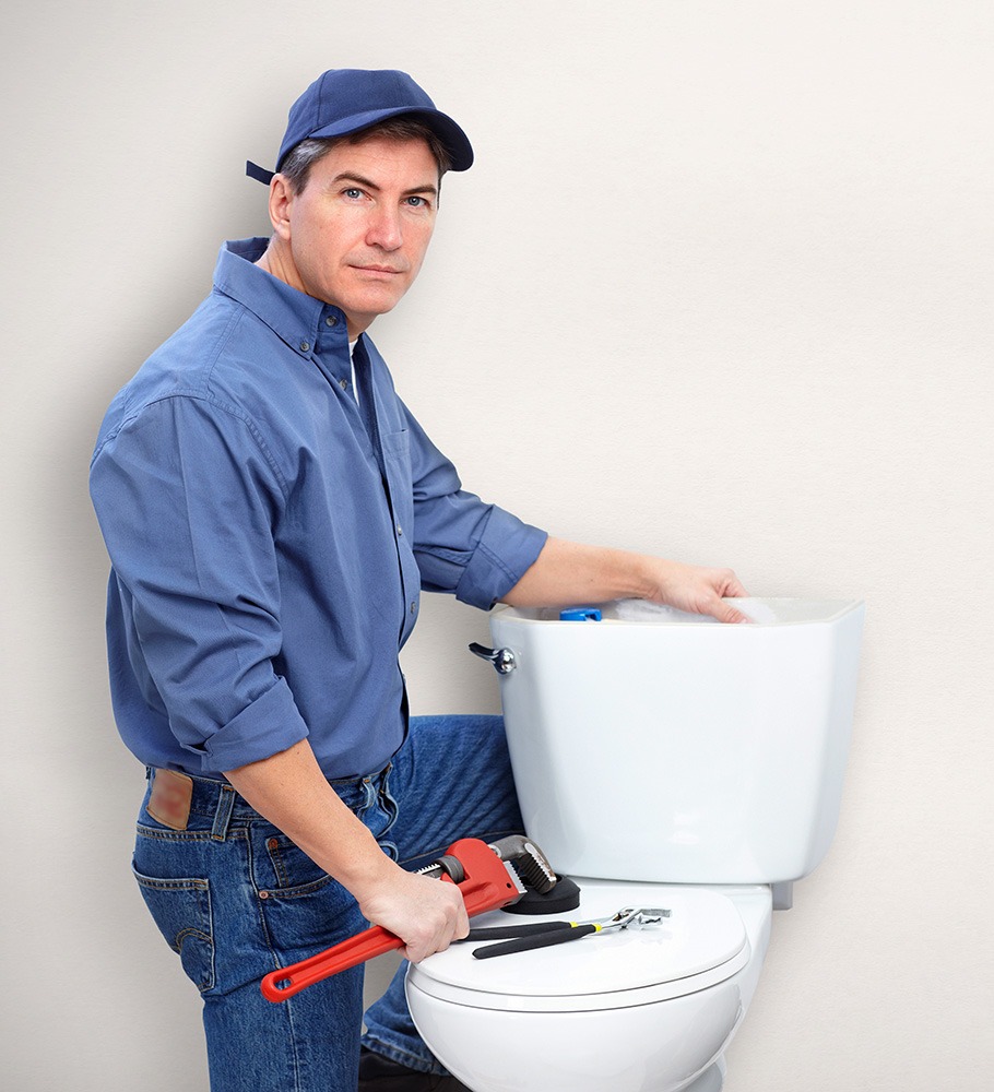 A plumber in a blue shirt and cap repairs a toilet tank, holding a wrench and other tools. The image emphasizes plumbing expertise and service.