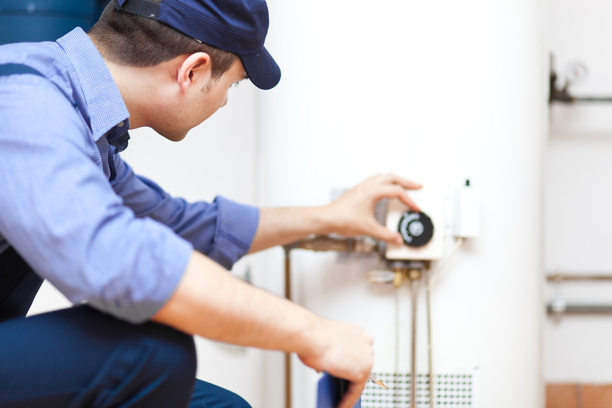 Plumber adjusting the temperature control on a water heater, demonstrating maintenance of home plumbing systems for efficiency and safety.