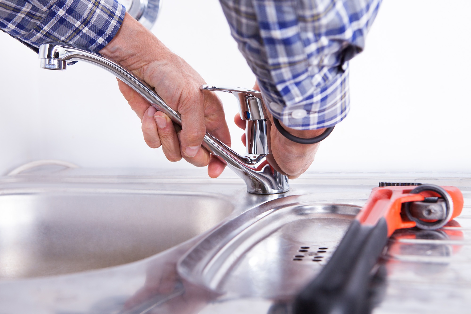A person installs a kitchen faucet, showing close-up detail of their hands adjusting the fixture. Tools are visible on the counter, highlighting the DIY nature of the task.
