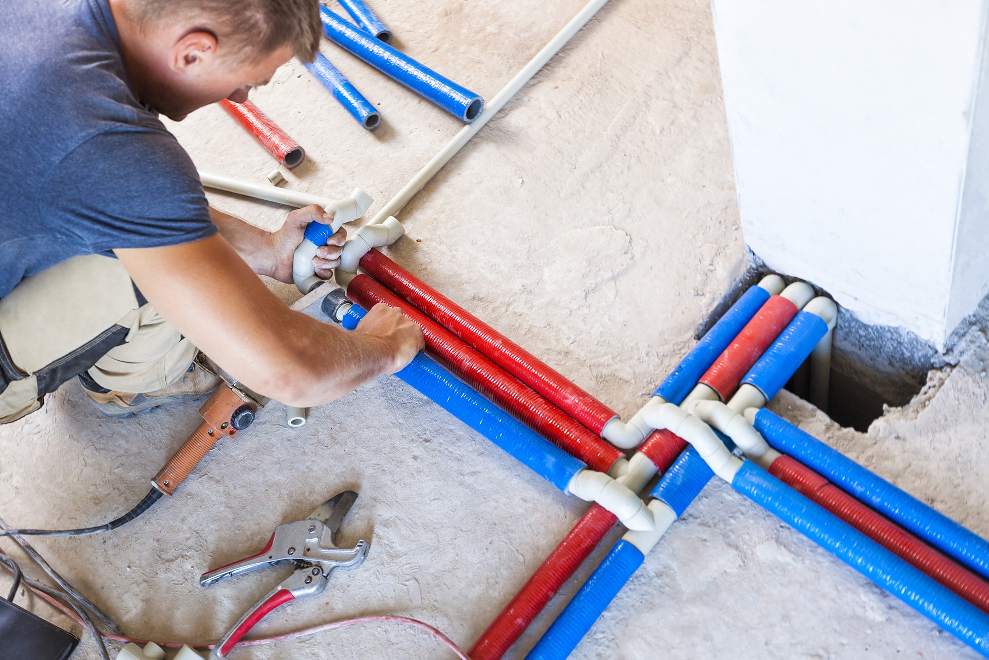 A plumber installs red and blue pipes during a construction project, ensuring proper connections for plumbing systems. Tools are visible nearby.