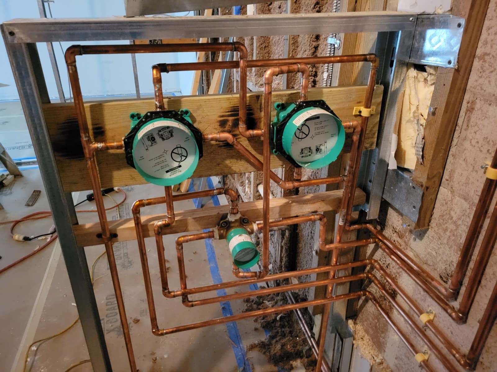 Copper plumbing installation with two water meters connected to a complex network of pipes on a wooden framework. Relevant for home renovation projects.