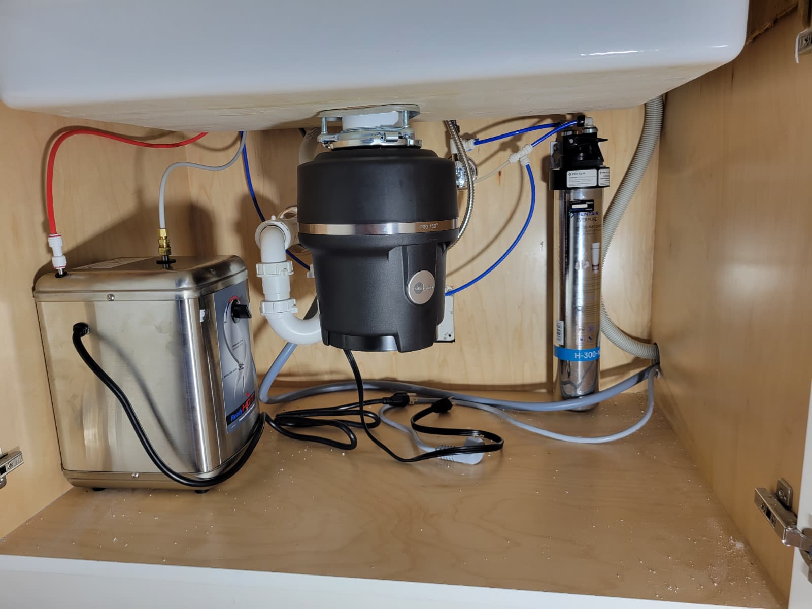 Under-sink setup featuring a garbage disposal unit, water filtration system, and connected plumbing. Relevant for home maintenance guides.