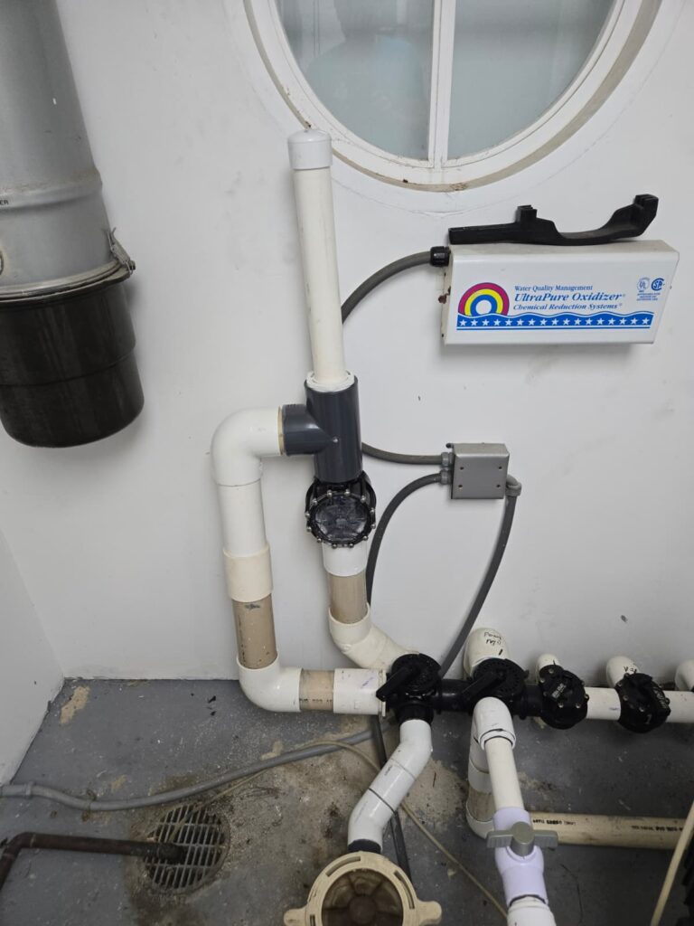 Pipes with valves are connected in a corner, with a control box labeled "UltraPure Oxidizer" above. A circular window is visible in the background.